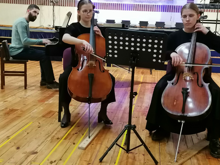 Priekšplānā divas čellistes. Fonā pianists.